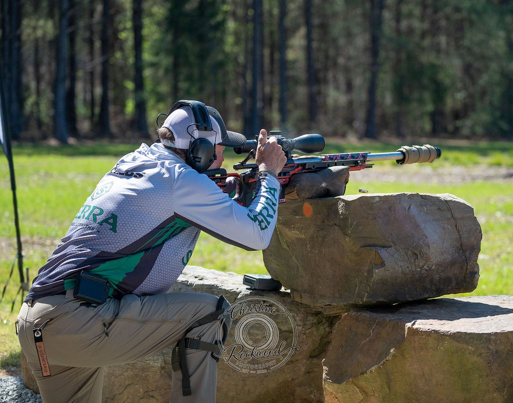 Shooter engaging a target from a rock barricade during a precision rifle competition.