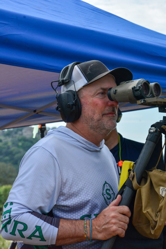 Precision rifle competitor observing downrange conditions through binoculars