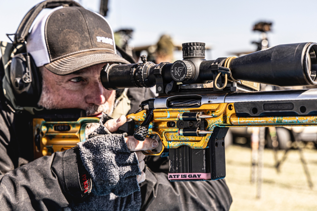 Precision rifle shooter aiming through a riflescope at a shooting match