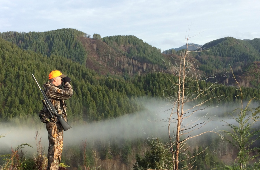 Hunter glassing mountain terrain from an elevated position.